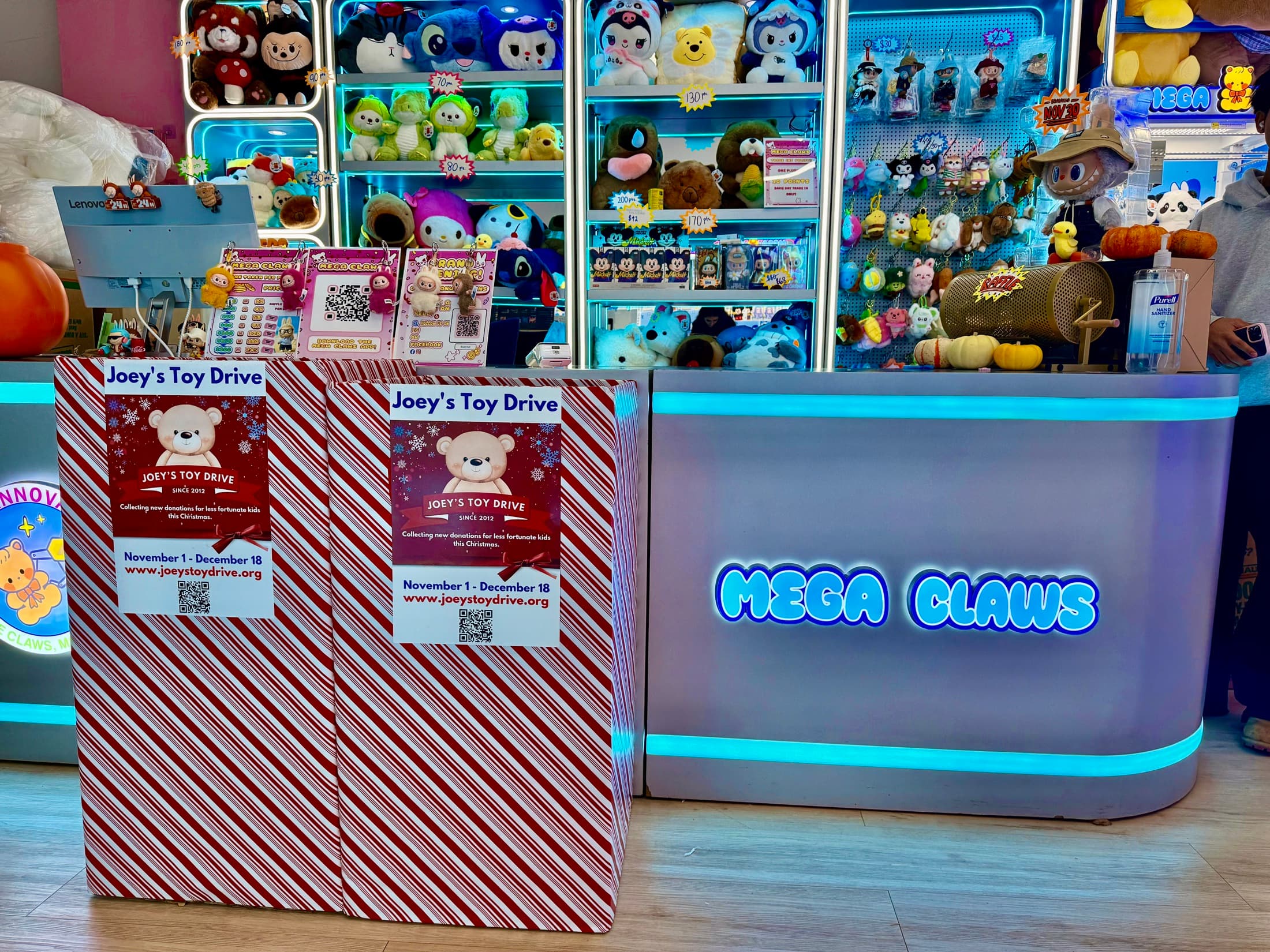 Two candy-striped Joey's Toy Drive collection boxes beside the prize counter of an arcade
