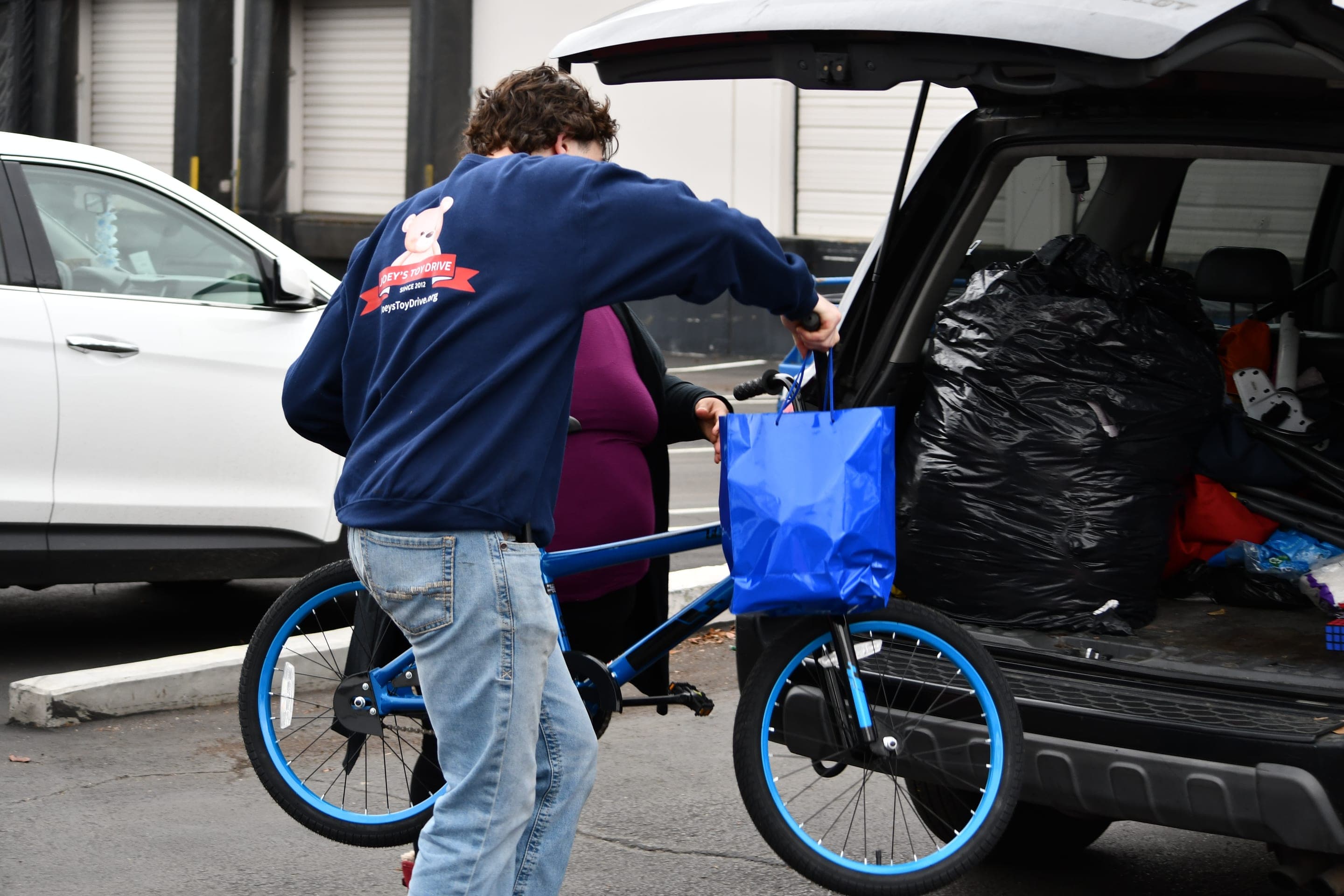 A Joey's Toy Drive volunteer loading a donated bike and bags of toys into a vehicle for delivery