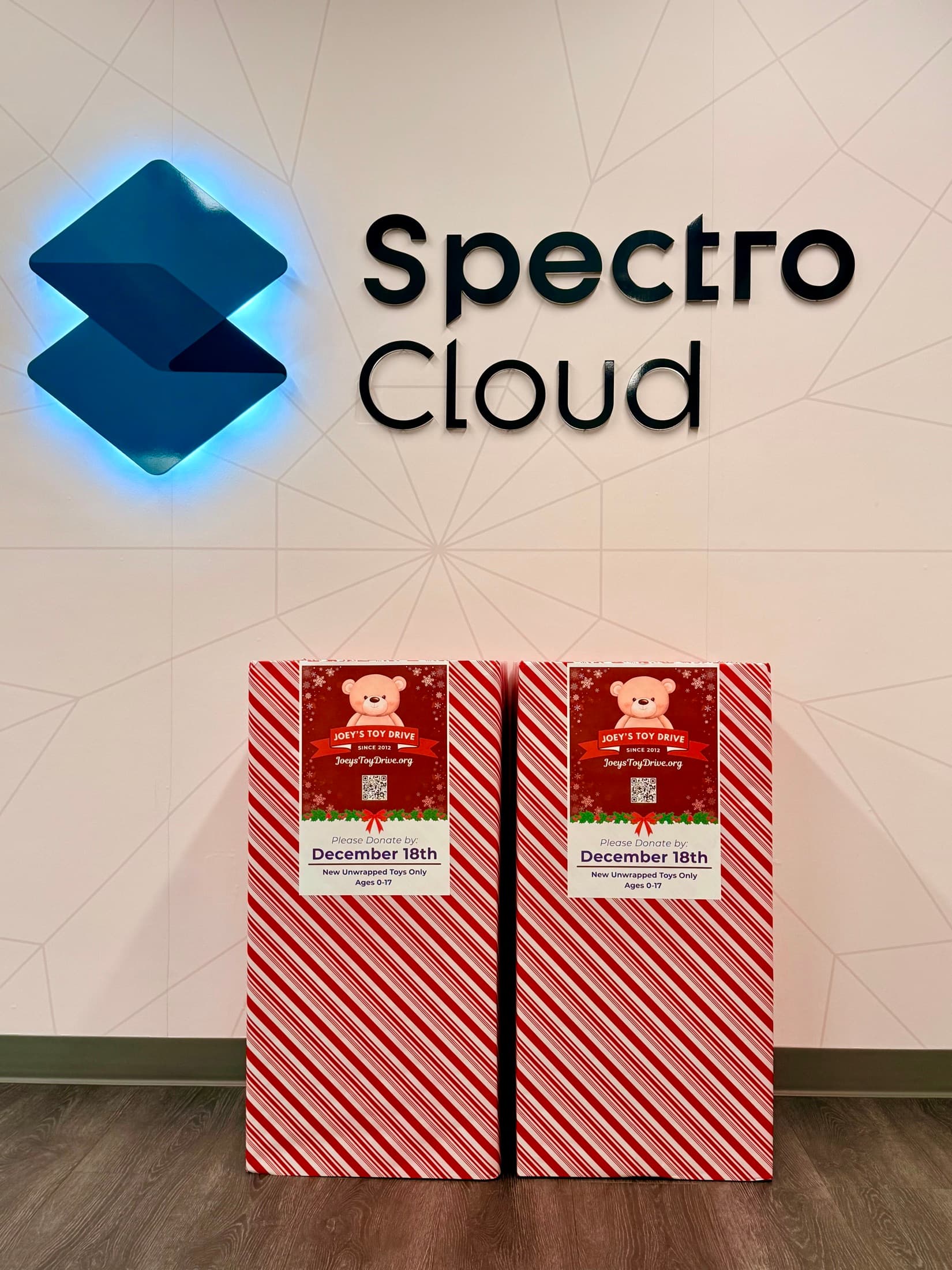 Two Joey's Toy Drive collection boxes beneath a software company's glowing lobby sign