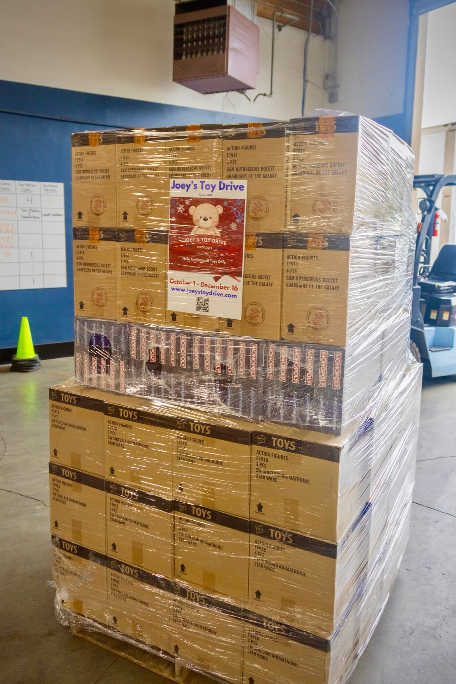 A shrink-wrapped pallet of boxed toys standing in a warehouse, a forklift behind it
