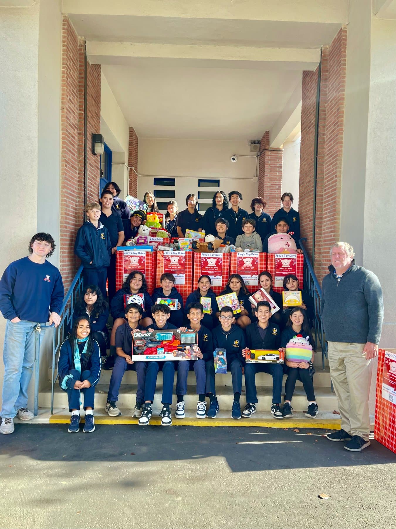 A school group gathered on the front steps around Joey's Toy Drive collection boxes filled with donated toys