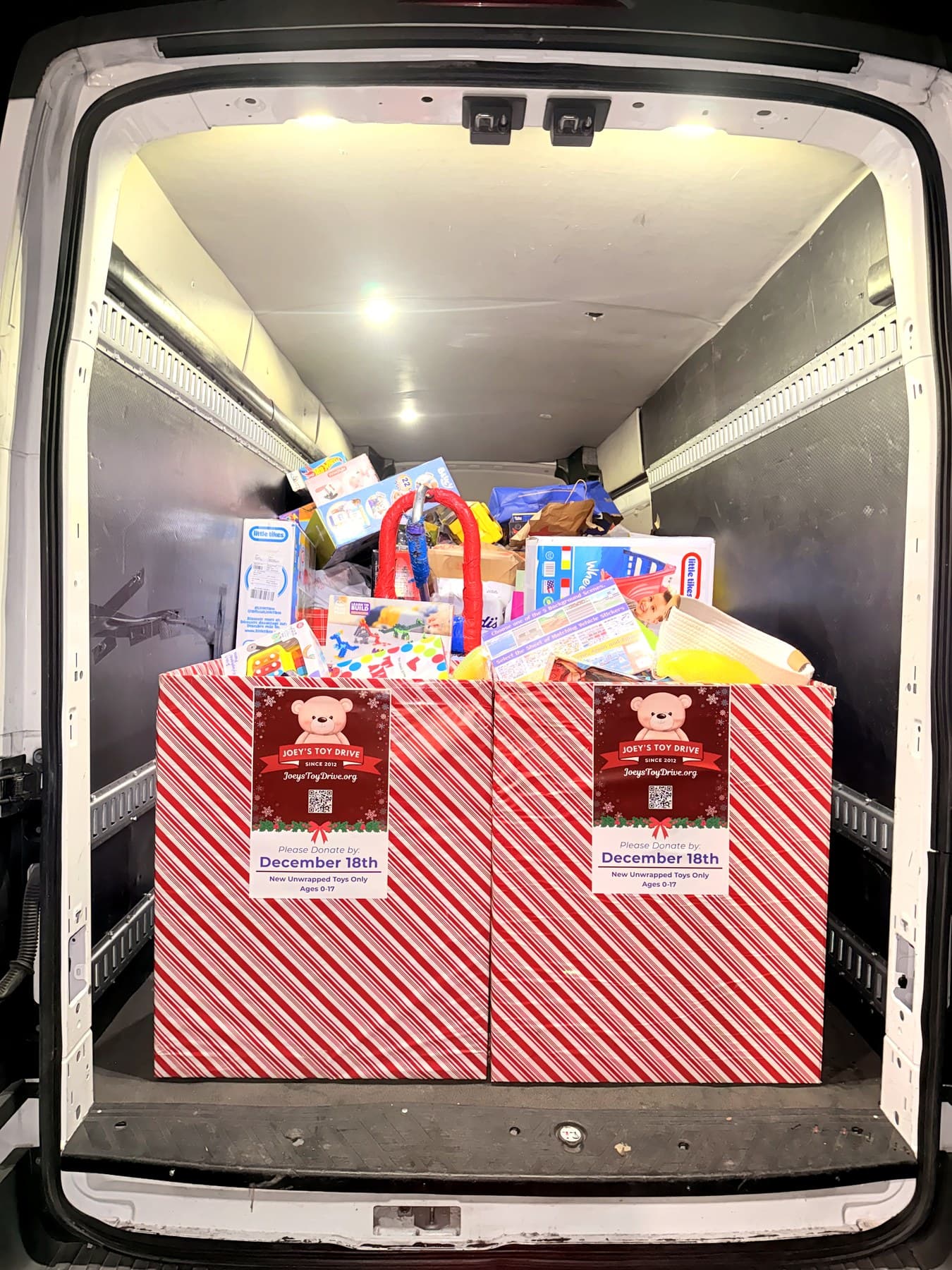 The open back of a moving van holding two candy-striped Joey's Toy Drive collection boxes stacked over the top with donated toys