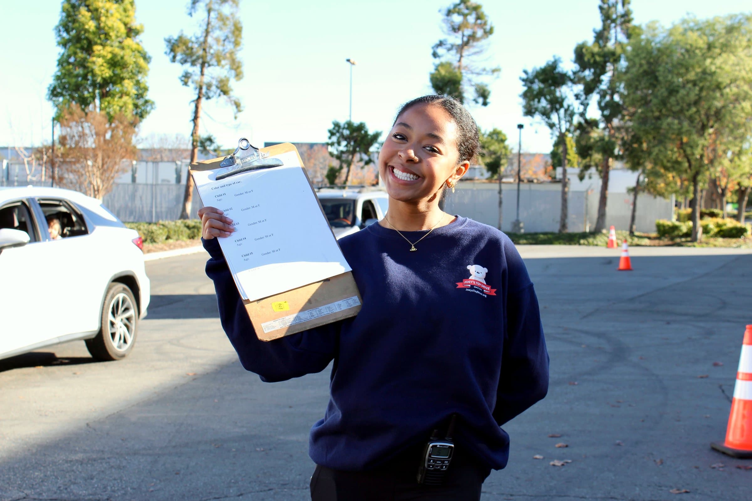 A smiling Joey's Toy Drive volunteer holding a clipboard at a Bay Area toy distribution