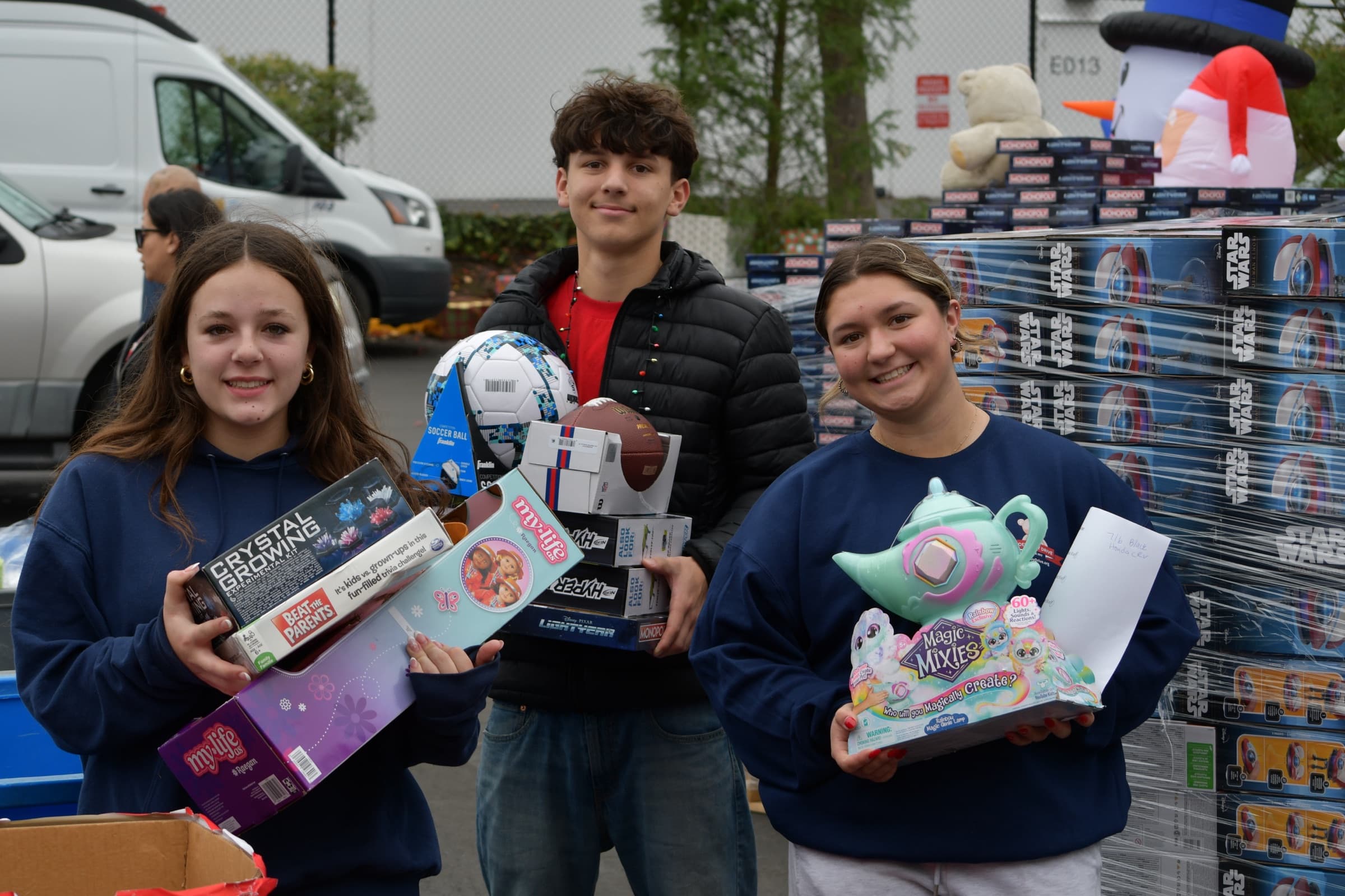 Three volunteers holding donated toys beside a loaded van.